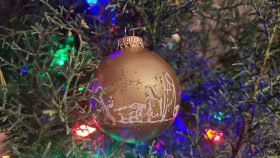 Christmas bulb with nativity scene on green Christmas tree.