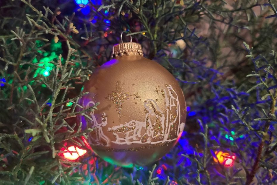 Christmas bulb with nativity scene on green Christmas tree.