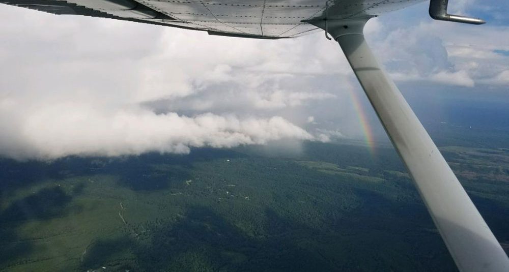 Looking out from a plane over green lush fields with a rainbow aginst a white cloud loud